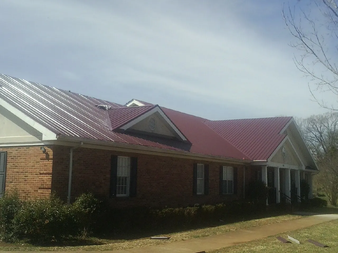 Red metal roof with gabled entries on a long brick building, from a Hail Damage Roof Repair job in Salina