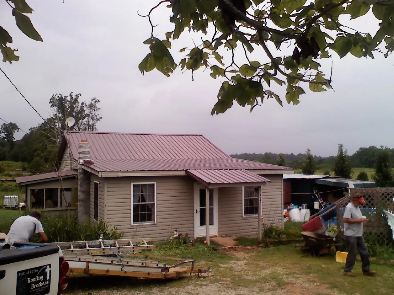 Crew finishing a mauve metal roof on a small farmhouse in Salina